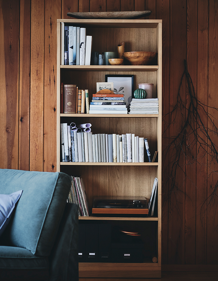 Wooden bookshelf with books, decorative bowls, and a record player, against a wood-panelled wall next to a blue sofa.
