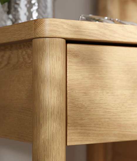Close-up of the rounded corner of a light wood side table with a smooth finish.