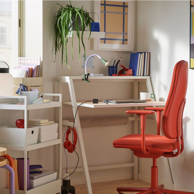 Bright and modern study space with white desk, red ergonomic chair, and colorful decor, perfect for working or studying at home.
