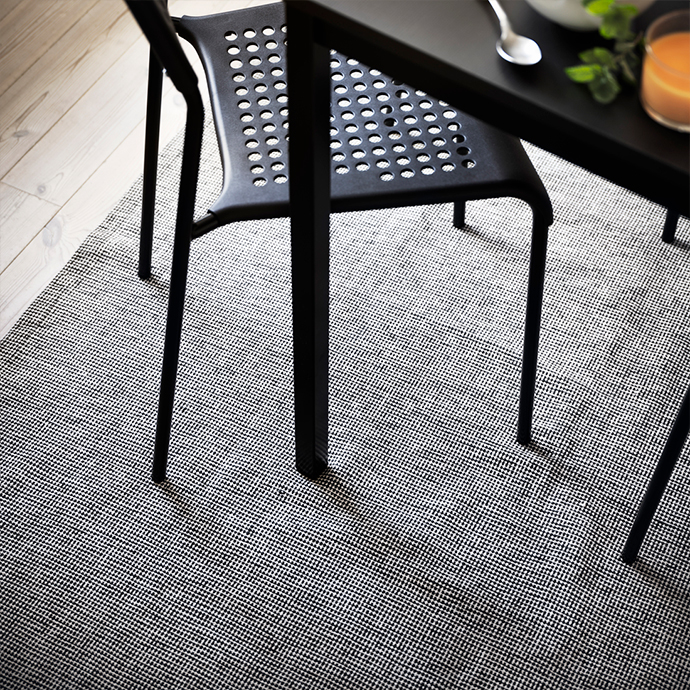 Two-tone geometric pattern rug under a black dining table and chairs with slender legs, on a light wood floor, creating a modern and functional ambiance.