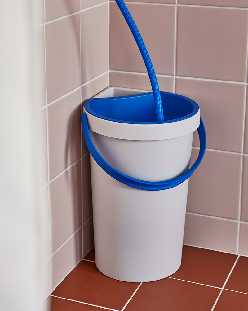 An 8-litre BERGVATTNET bucket with a hose attached to it is sitting in the corner of a tiled shower space.