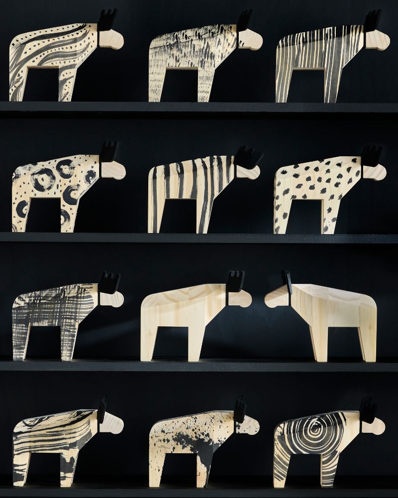 A shelf displays twelve carved wooden moose figures with various black and white patterns, and some are unpainted.