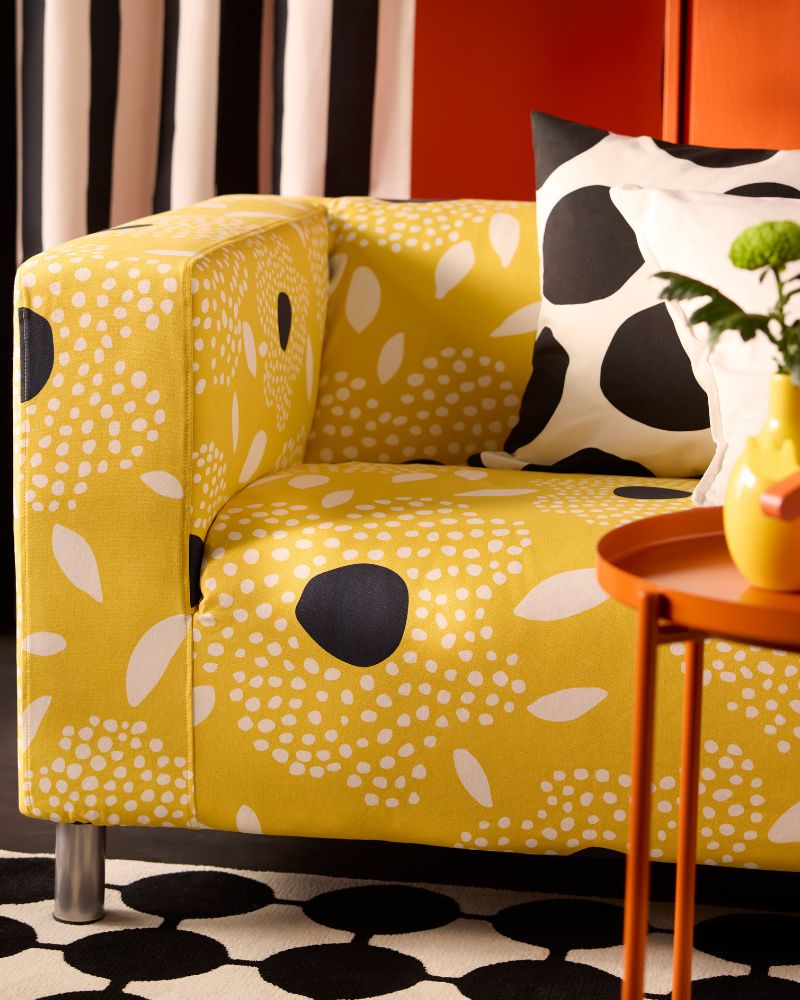 A modern sofa in yellow with white and black patterns, with a black and white cushion. Red wall and striped curtains.