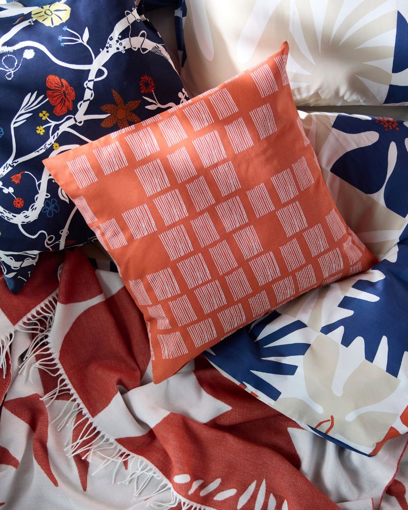 Close-up of a stack of pillows and a blanket with various patterns, including orange, blue, and red floral designs.