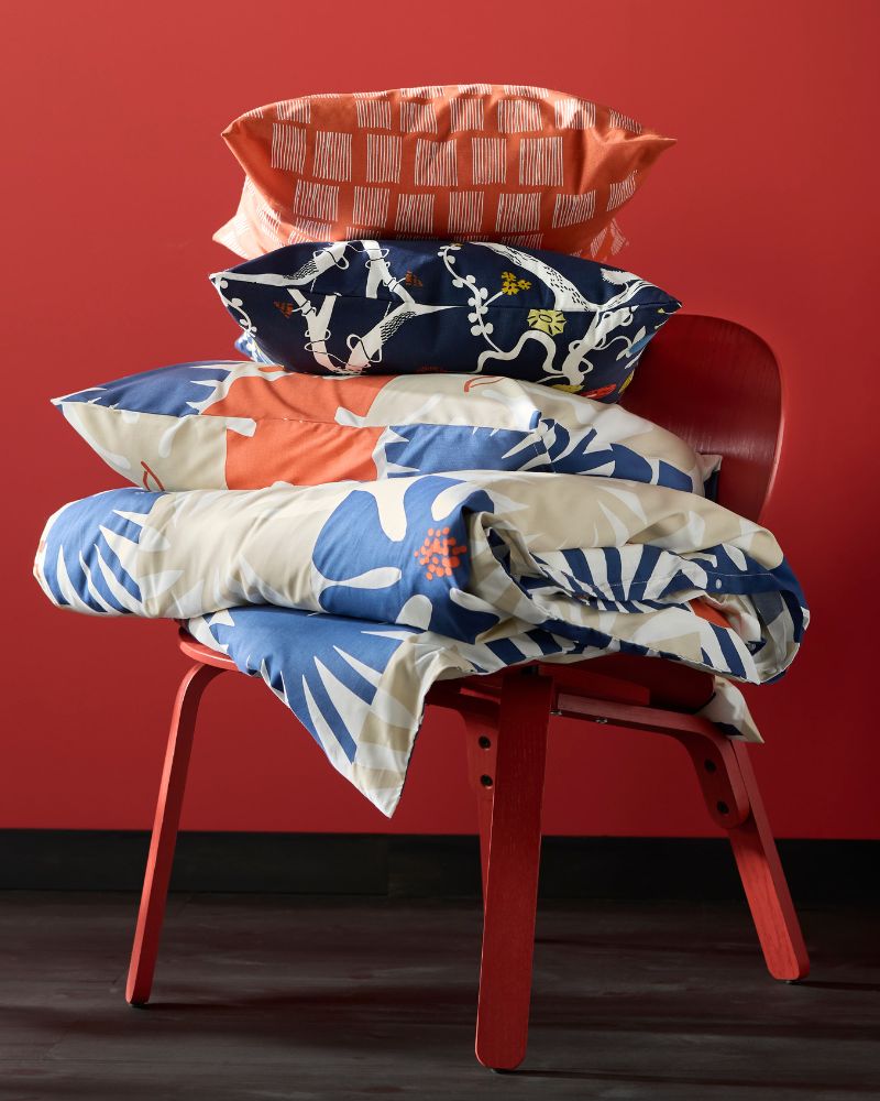A stack of colorful pillows and a duvet, featuring orange, blue, and red patterns, rests on a red chair.
