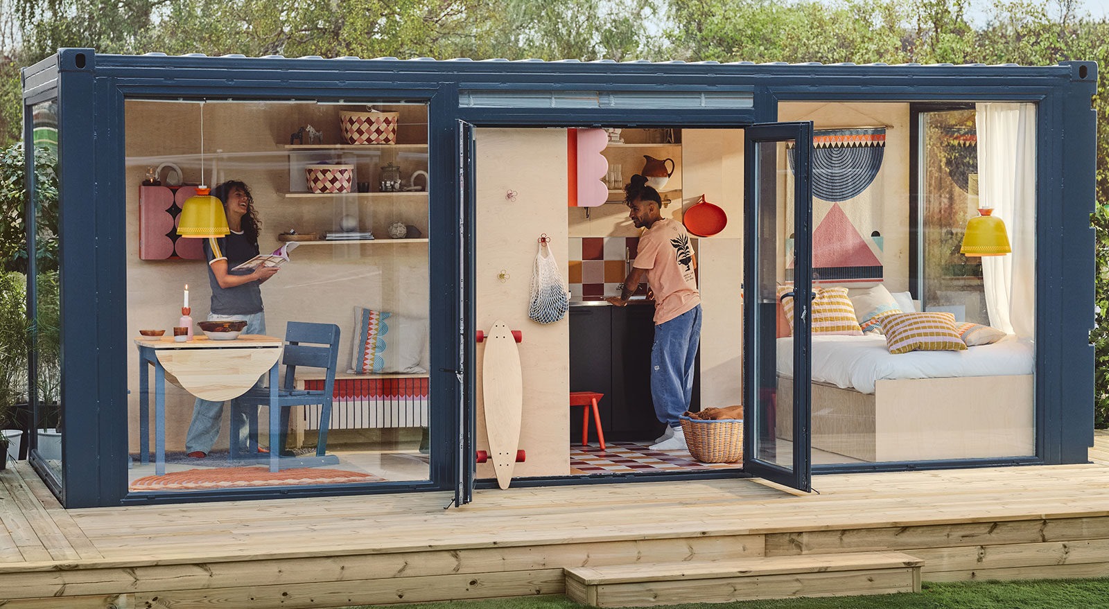 Small house made from shipping containers, with windows to the bedroom and living room; open door shows IKEA OMMJÄNGE items.