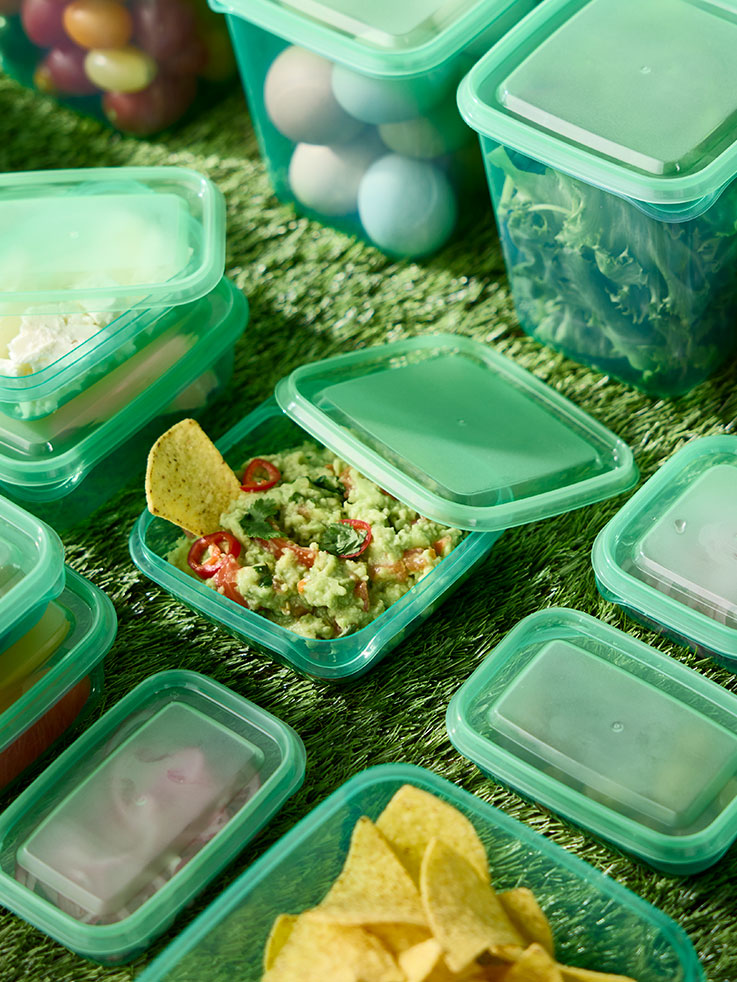 Several green PRUTA food containers with lids on a table. One open container filled with food has its lid resting against it.