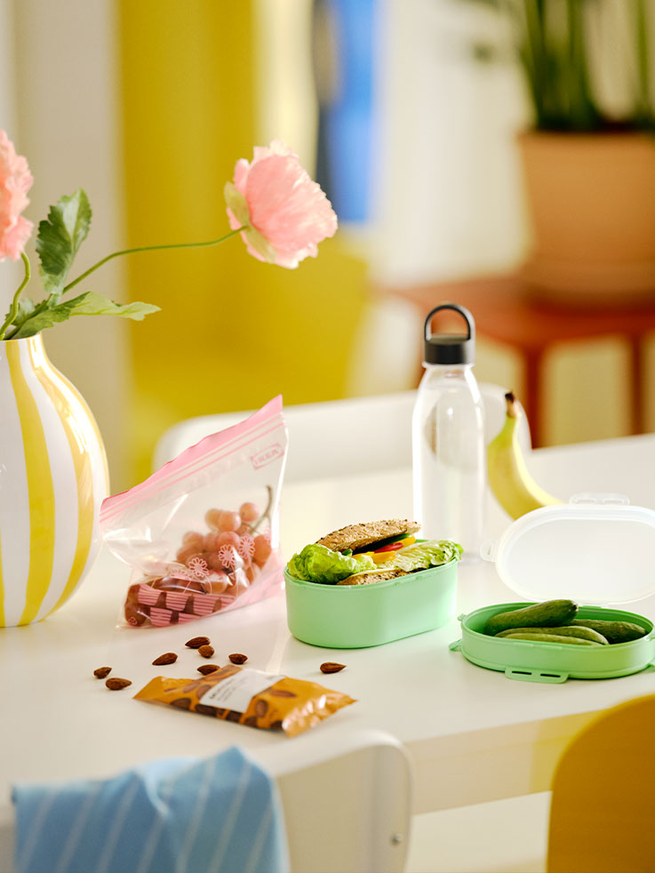 A table with IKEA 365+ water bottle in dark grey, UTBJUDA stackable lunch box in light green and MUNSBIT roasted almonds