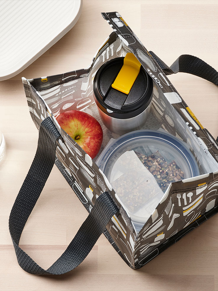 A table with diverse items, including an UNDERSÖKA insulated travel mug in black, a banana and a person holding a mug