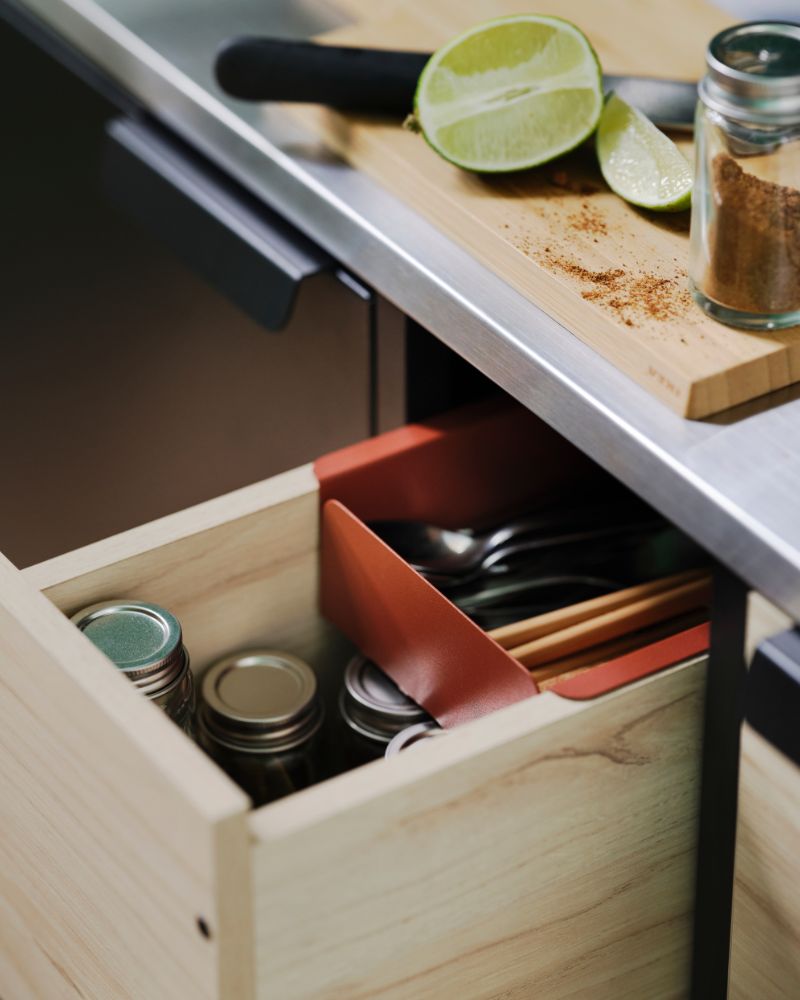 A close-up of a pulled-out ash drawer of an ÄSPINGE kitchenette. There are cutlery and small jars with lids in the drawer.