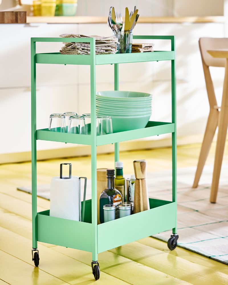 Light green NISSAFORS drinks trolley on wheels loaded with bowls, plates and other dinnerware in a modern kitchen setting.