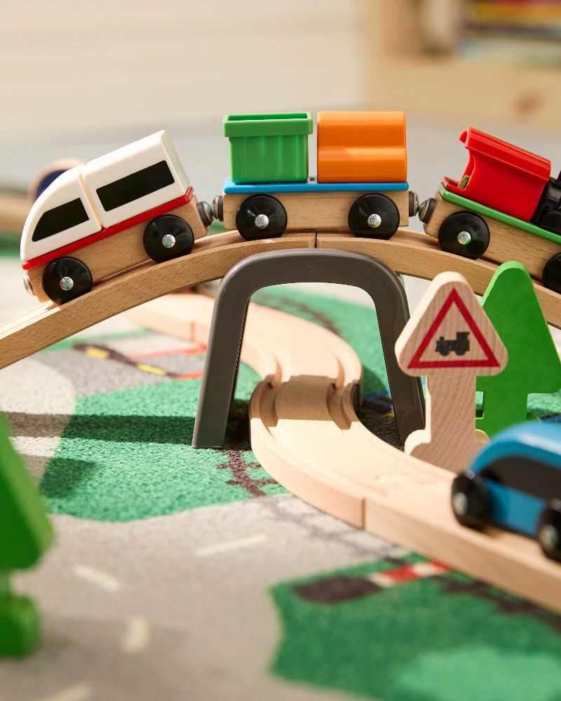 A toy train set with a red, white, green, and orange train on a wooden track and bridge.