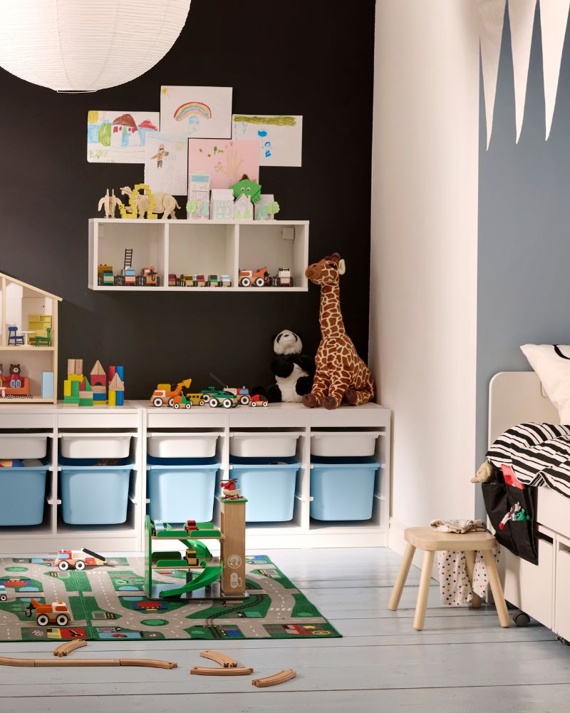 A colorful kids' playroom with a black wall, white toy storage with blue bins, a giraffe, and a road rug.