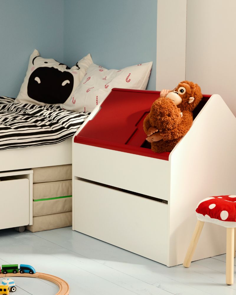 A child's bedroom with a white bed, black and white striped bedding, and plush toys on a blue wall.