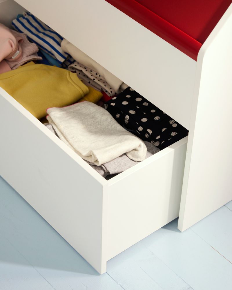 A close-up of a white drawer filled with colorful folded clothes, including yellow, white, and striped items.