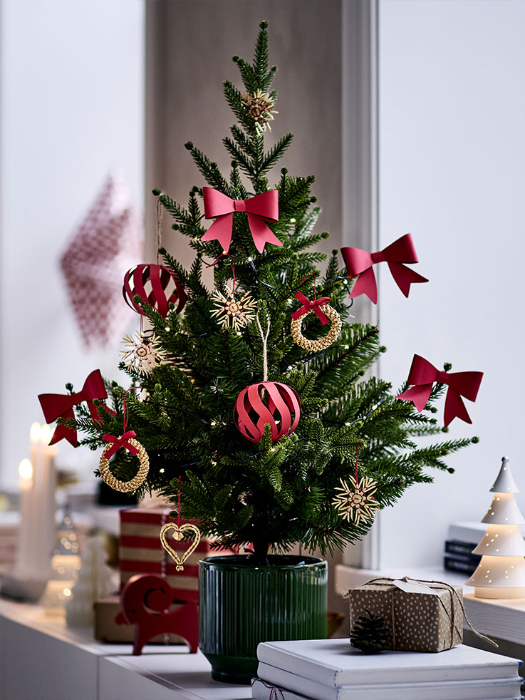 A small potted Christmas tree is decorated with red and gold VINTERFINT tree ornaments and is placed on a sideboard.