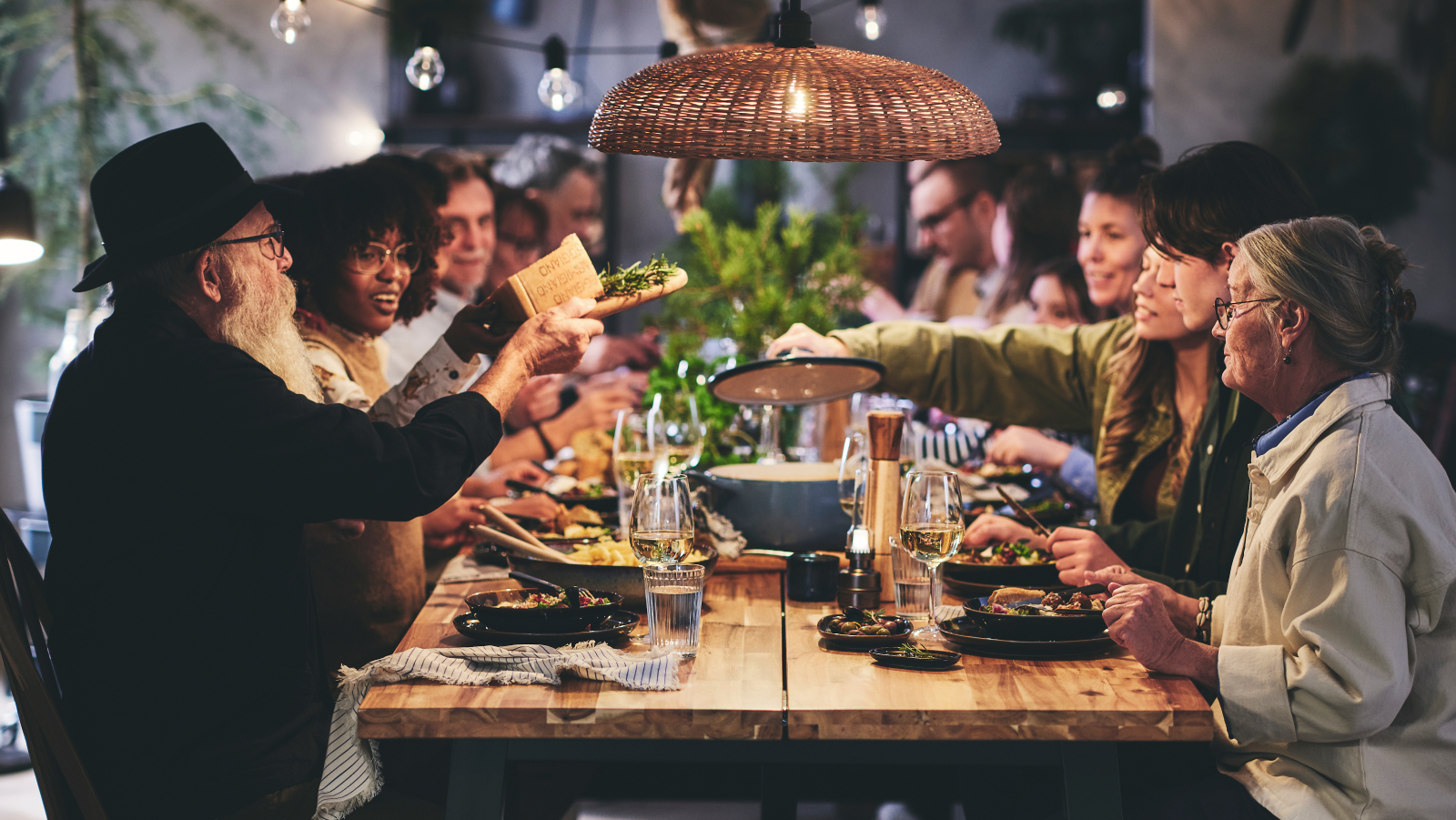 An elderly couple seated at the end of a long table surrounded by seated dinner guests of all ages.