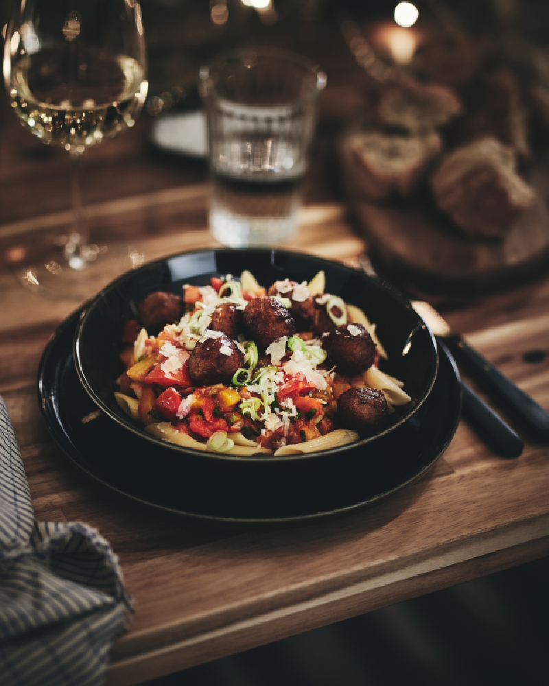 A dinner guest at a long table passes a bowl of HUVUDROLL plant balls to the guest sitting beside them.