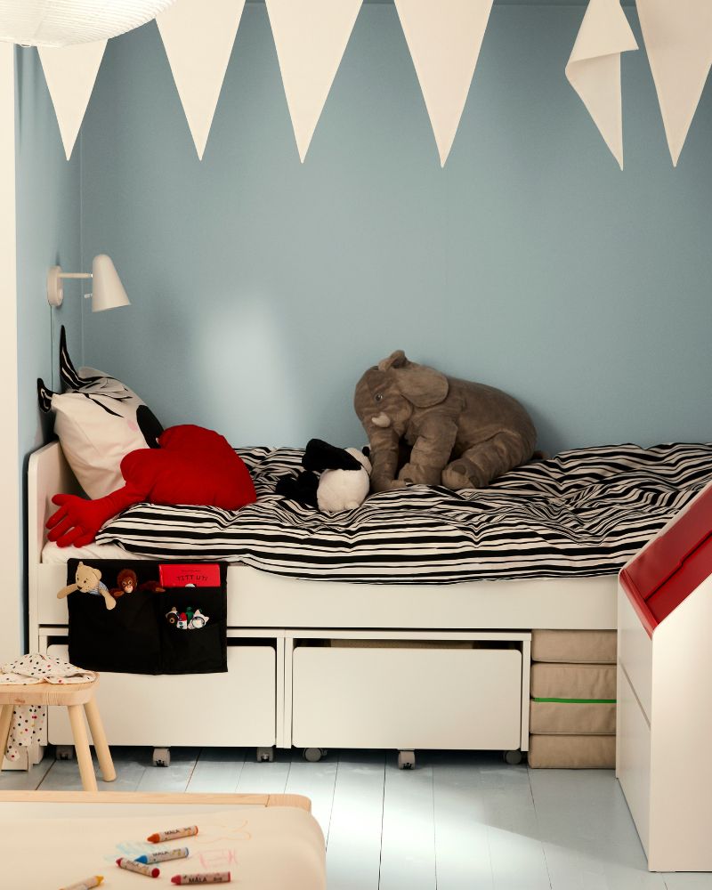 A white toy storage unit with a red lid, holding a plush monkey. A mushroom stool is nearby.