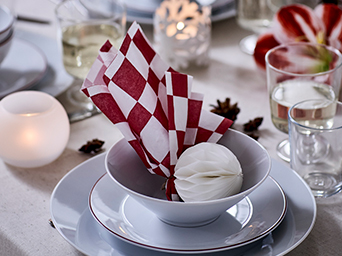 Detalle de mesa navideña, con vajilla blanca y servilleta roja a cuadros decorando