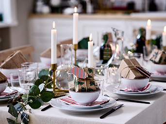 Mesa navideña decorada con velas y vajilla blanca con regalos para cada comensal sobre los platos