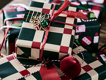 Primer plano de regalos de Navidad envueltos en papel estampado a cuadros rojo, verde y beige, atados con cintas y adornos colgantes de copo de nieve.