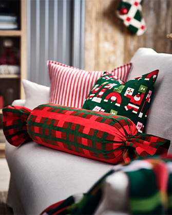 Sillón blanco de tela tapizada con una pila de tres cojines decorativos de Navidad en rojo y verde, incluyendo uno a rayas, otro con patrón de Santa y otro con forma de caramelo.