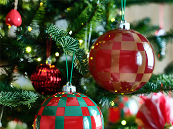 Detalle del árbol con bolas de Navidad grandes de vidrio o plástico en rojo y verde, con diseños a cuadros y patrones de caramelo, entre las ramas y luces LED.