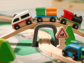 Tren de juguete de madera con vagones de colores cruzando un puente sobre vías de madera. Ideal para desarrollar habilidades motoras e imaginación durante el juego