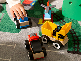 Niño jugando con camiones de juguete coloridos y vehículos de construcción sobre una alfombra de juego con caminos y espacios verdes