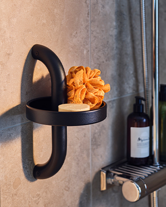 Black wall-mounted candle holder with curved handle holding an orange dried flower. Dark bottle visible in background