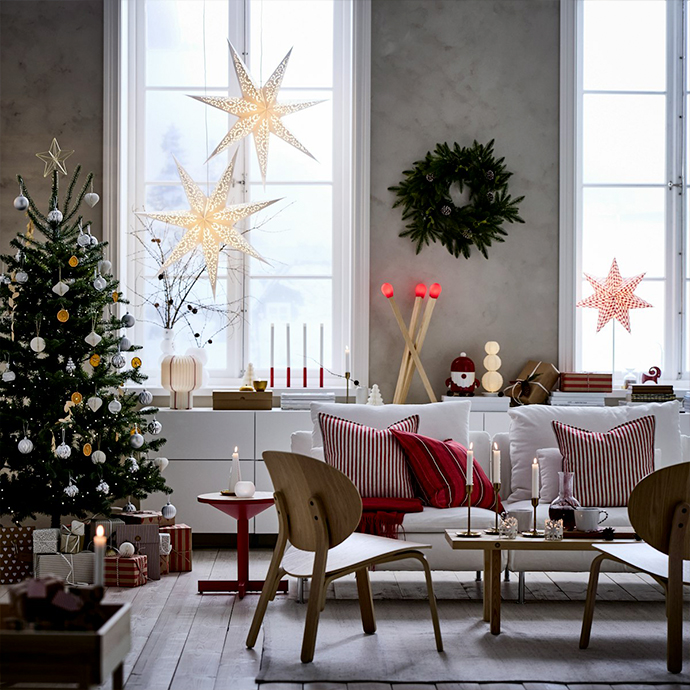 Living room with Christmas tree, paper star decorations in window, white sofa with red striped cushions, and wooden coffee table. Holiday decorating made simple with lights and natural materials