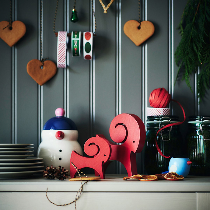 Decoraciones navideñas en estante de cocina con galletas de jengibre en forma de corazón, renos rojos de madera, tarro de cerámica con muñeco de nieve, recipientes de vidrio con cintas festivas y ramas de pino