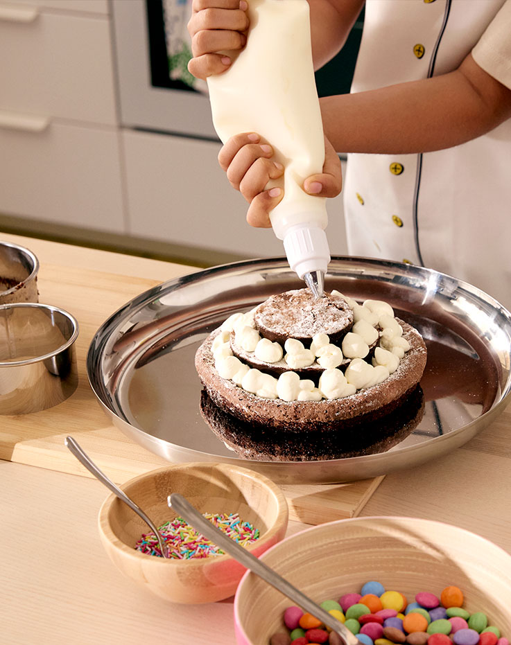 A chocolate cake in three layers, being decorated with little dots of cream with the help of SMAKSAM piping tool.