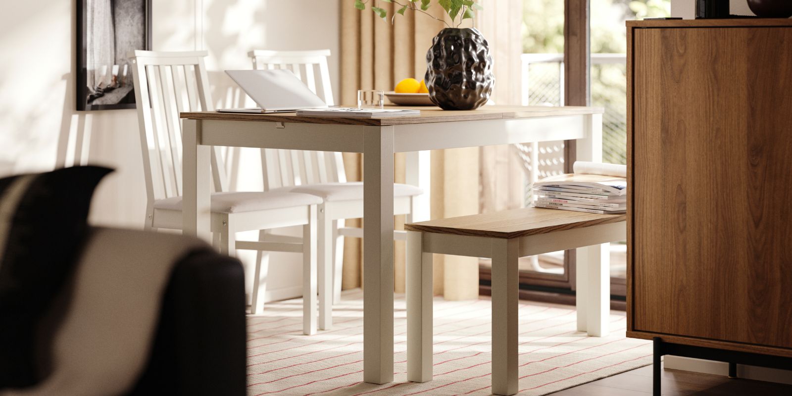 A dining area has a beige/brown ÅLHULT extendable table with a bench on one side and two chairs with soft seats on the other.