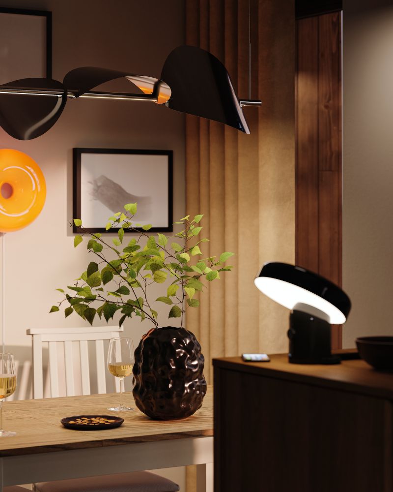 A black STOCKHOLM vase is standing on a table in a cosy dining area with several lamps, creating a soft atmosphere.