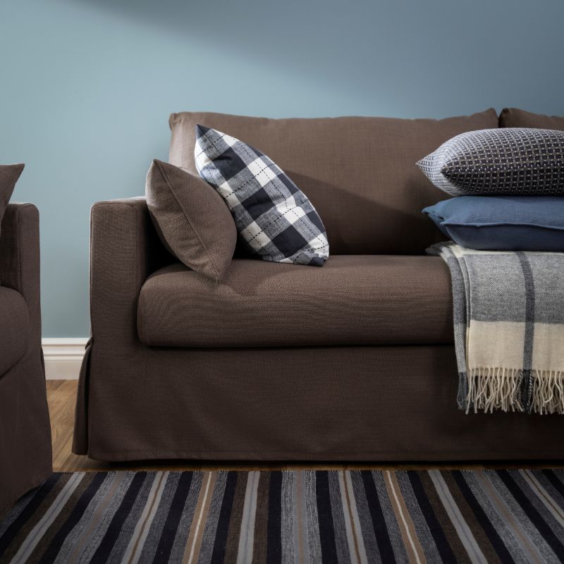 A cushion with a chequered SVAMPFLY cushion cover lies on a HYLTARP 3-seat sofa near some other cushions and a throw.