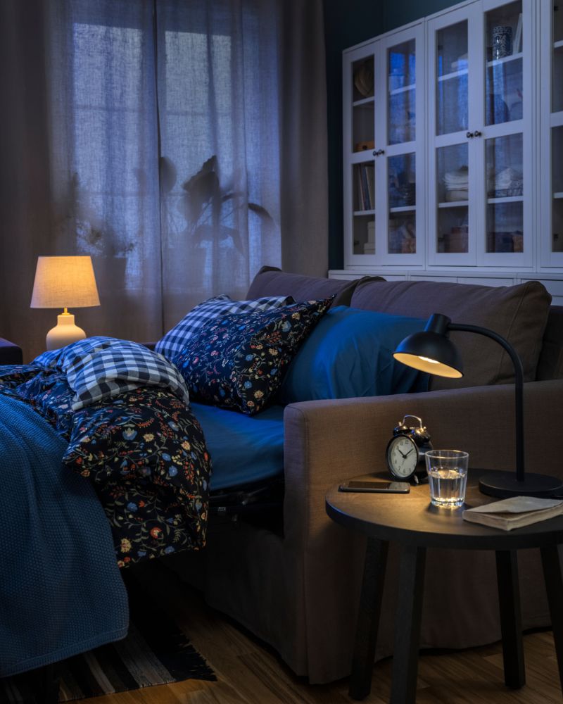 A HYLTARP sofa-bed, configured as a bed and with BRUDKRUSBÄR bed linen, stands in front of some HAVSTA storage combinations.