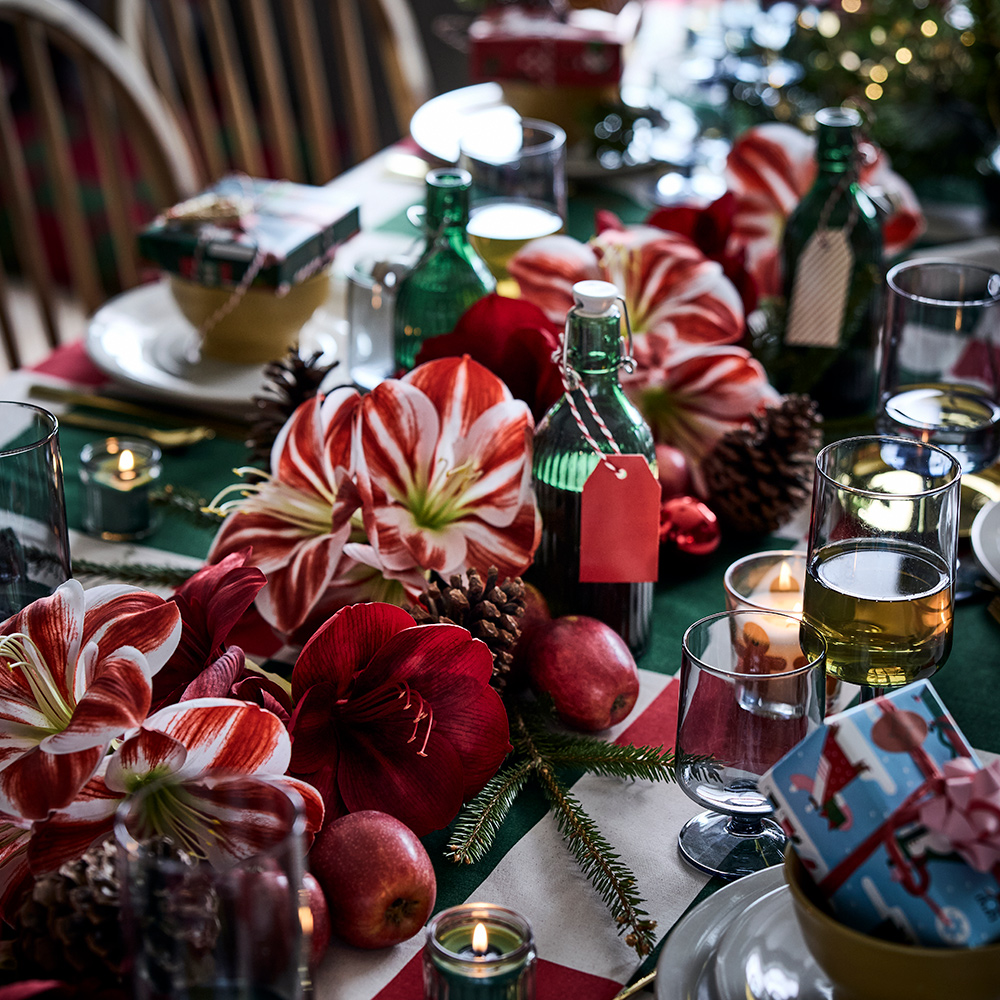 Christmas table with a VINTERFINT artificial flower, OMBONAD glasses, SANDSKÄDDA bowls, VINTERFINT scented candles, and VINTERFINT bottles with lids.