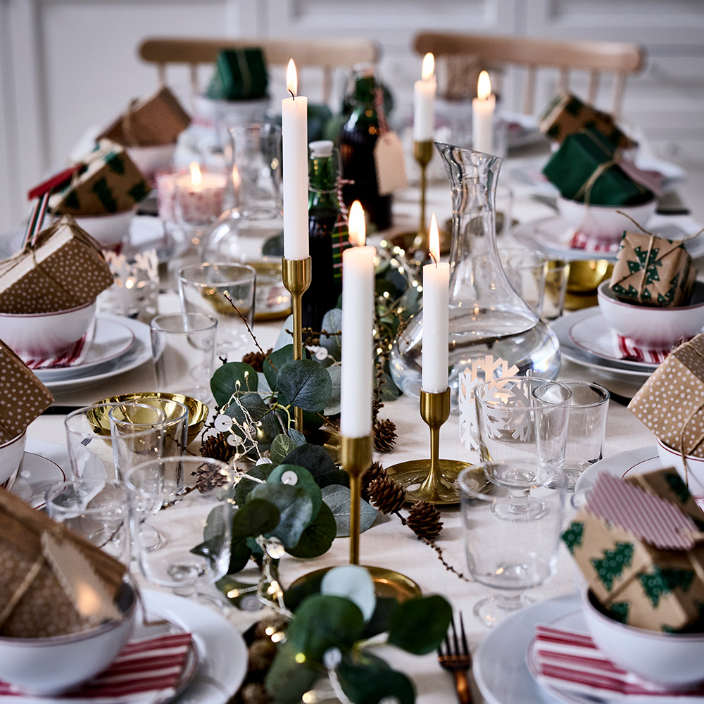 A table decorated for Christmas with VINTERFINT bowls, OFTAST plates, unscented JUBLA candles, STORSINT and STOCKHOLM 2025 decanters, and a VINTERFINT tablecloth.