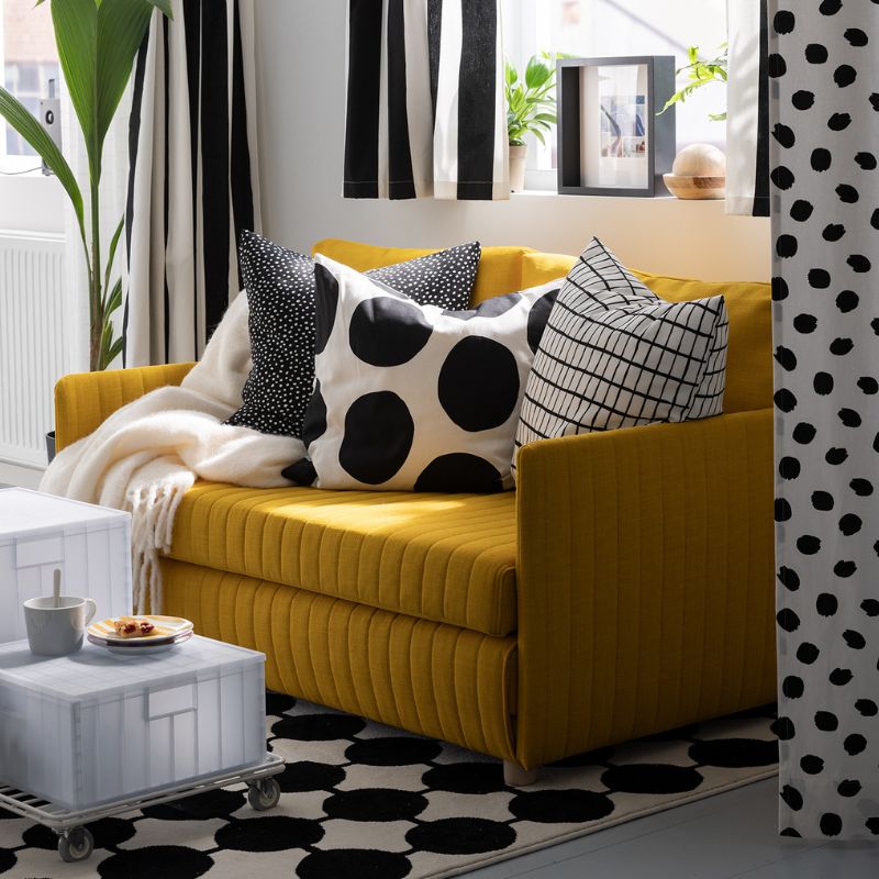 A throw and three cushions, including one with a BLÅMUNKAR cushion cover with large black dots, lie on a FRIDHULT sofa-bed.