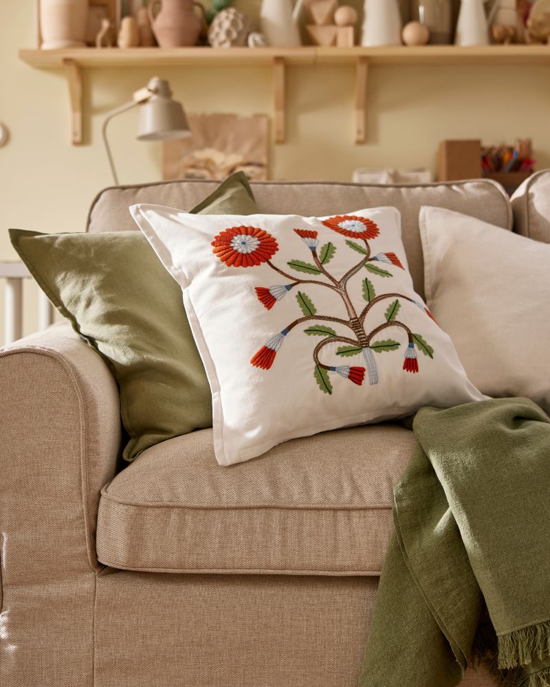 A DYTÅG throw and three cushions, including one with a flowery FACELIOR cushion cover, lie on an EKTORP sofa.