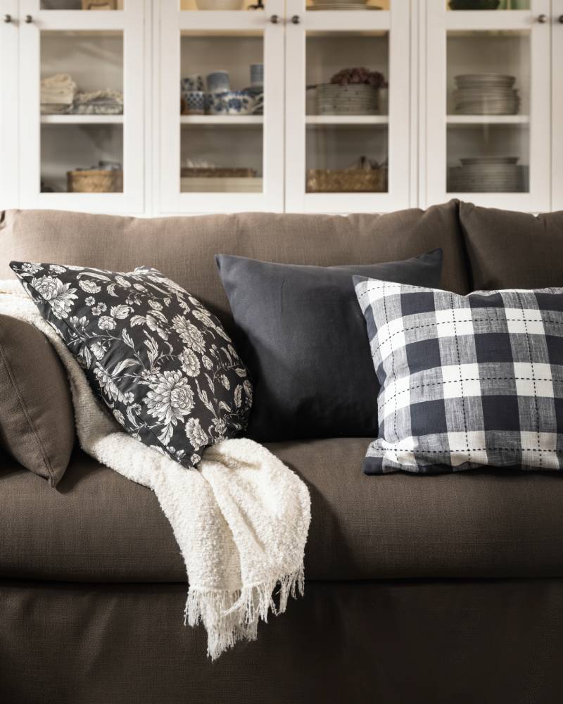 An off-white SANDBRODD throw and some cushions, including one with a floral IDALINNEA cushion cover, lie on a HYLTARP sofa