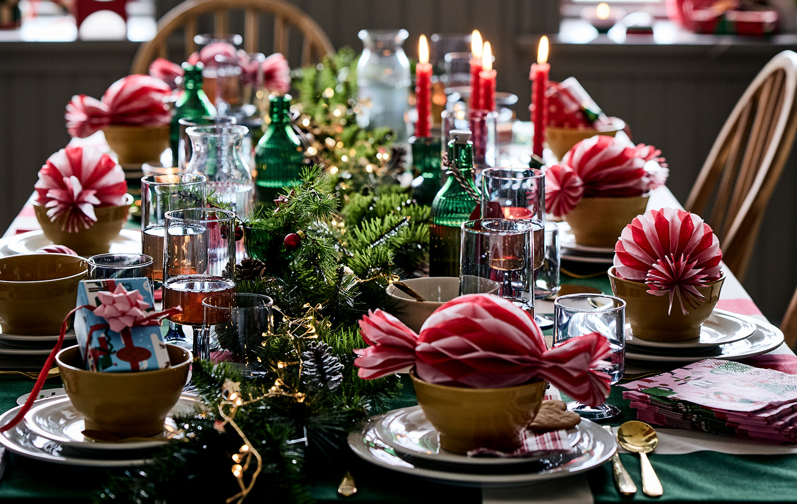A Christmas table with VINTERFINT tree ornaments, VINTERFINT bottle with cork, VINTERFINT artificial mistletoe, SANDSKADDA bowl and SANDSKÄDDA plates, plus FÖRNUFT cutlery set and yellow SKOGSTA chairs.