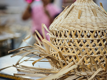 Una pantalla de lámpara colgante MÄVINN a medio terminar está sobre una mesa. Las tiras de fibra de plátano sobresalen en todas direcciones.