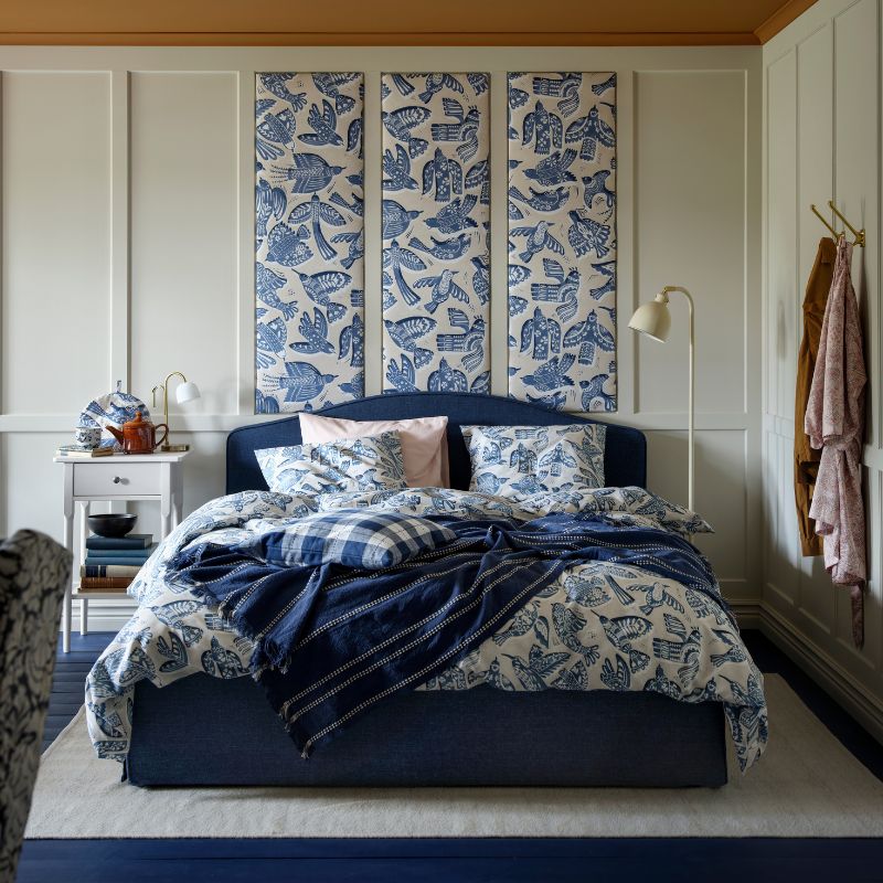 A dark blue RAMNEFJÄLL upholstered bed frame together with a BITTERSÖTA duvet cover and pillowcase set and pre-cut fabric
