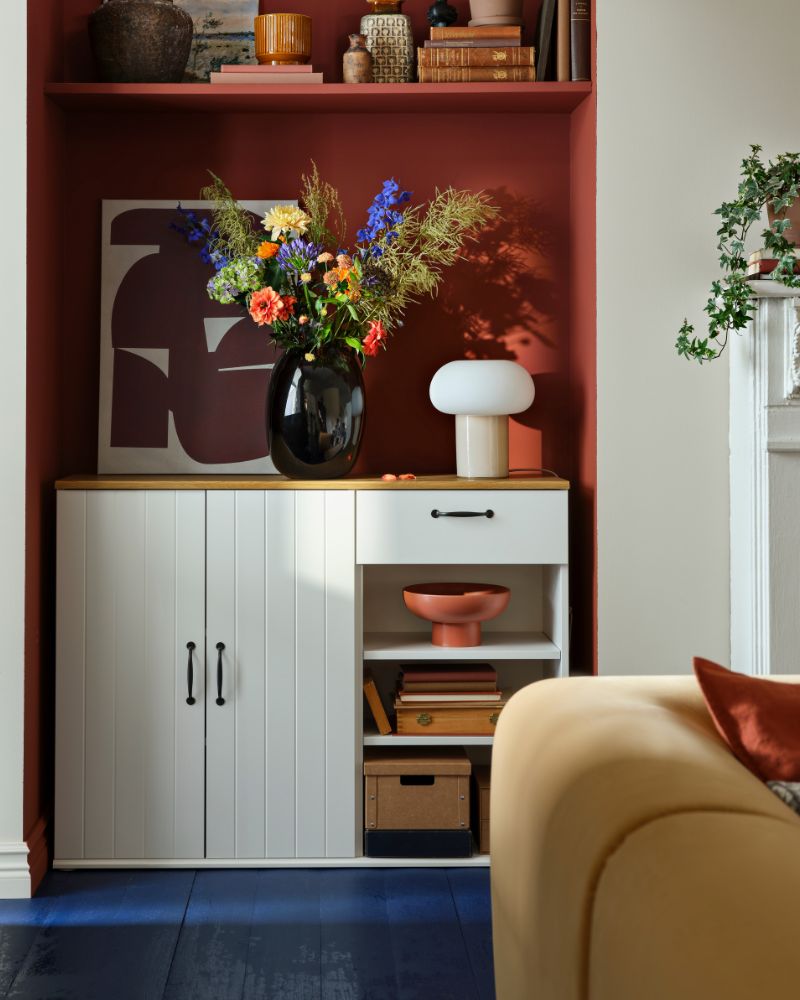 A white SKRUVBY sideboard with two cabinets and a drawer, decorated with flowers and a vase in a stylish interior.