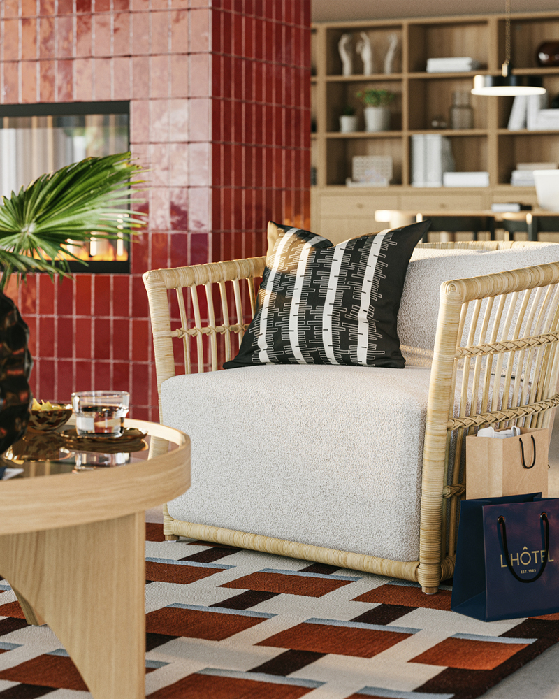 A close-up on STOCKHOLM 2025 grey/white armchair next to a round coffee table in a spacious hotel lobby by a fireplace.