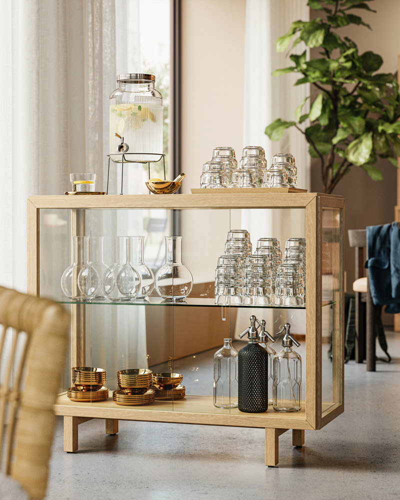 A natural oak veneer STOCKHOLM 2025 glass-door cabinet in a hotel lobby that creates a drink station with refreshments.
