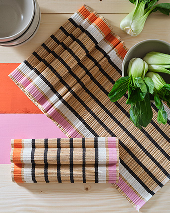 Dos caminos de mesa MÄVINN yacen sobre una mesa de madera pintada. La mesa también tiene cuencos de cerámica y vegetales verdes.